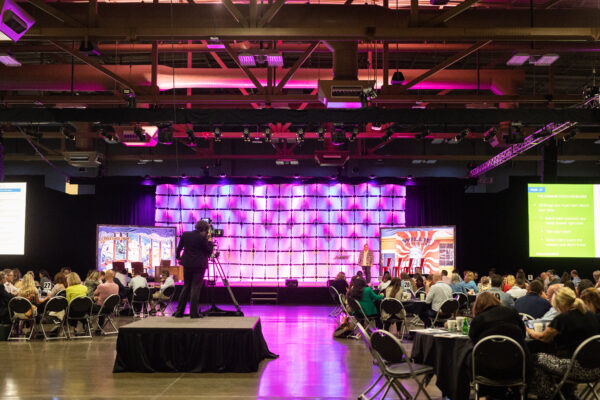 large general session room with a purple and pink uplight stage with local Austin, TX scenics
